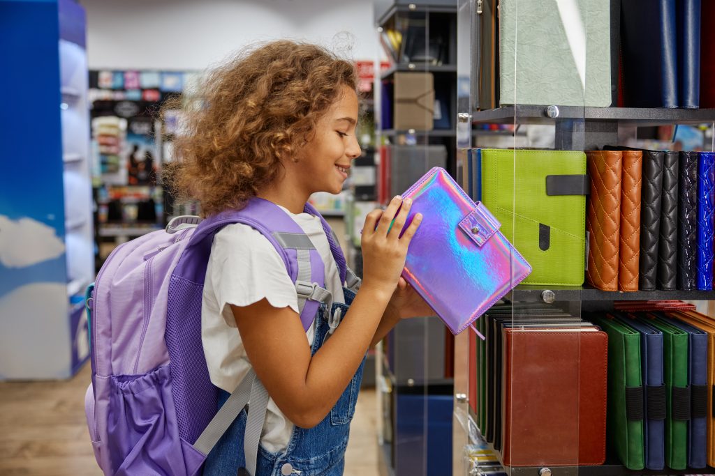 una nina feliz y emocionada buscando suministros escolares en una tienda de papeleria